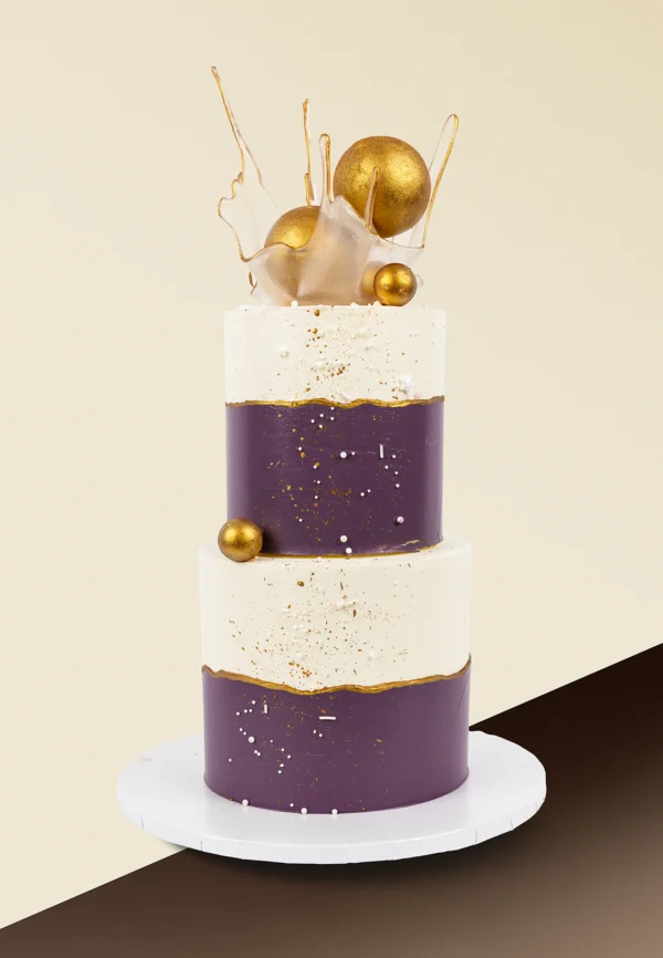 Dwupiętrowy tort w kolorach bieli i fioletu ze złotymi dekoracjami i abstrakcyjnym topperem z karmelowego szkła – elegancki tort okolicznościowy dla dorosłych