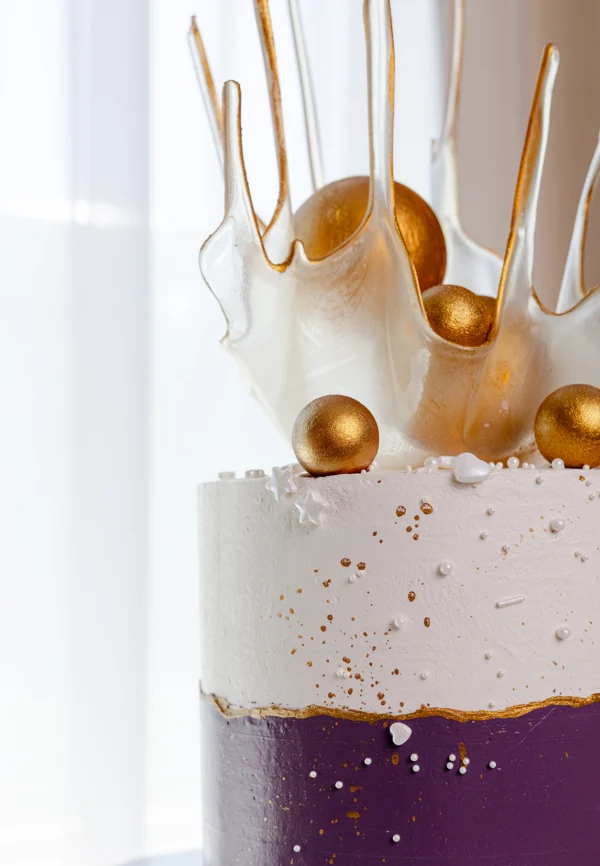 Dwupiętrowy tort w kolorach bieli i fioletu ze złotymi dekoracjami i abstrakcyjnym topperem z karmelowego szkła – elegancki tort okolicznościowy dla dorosłych
